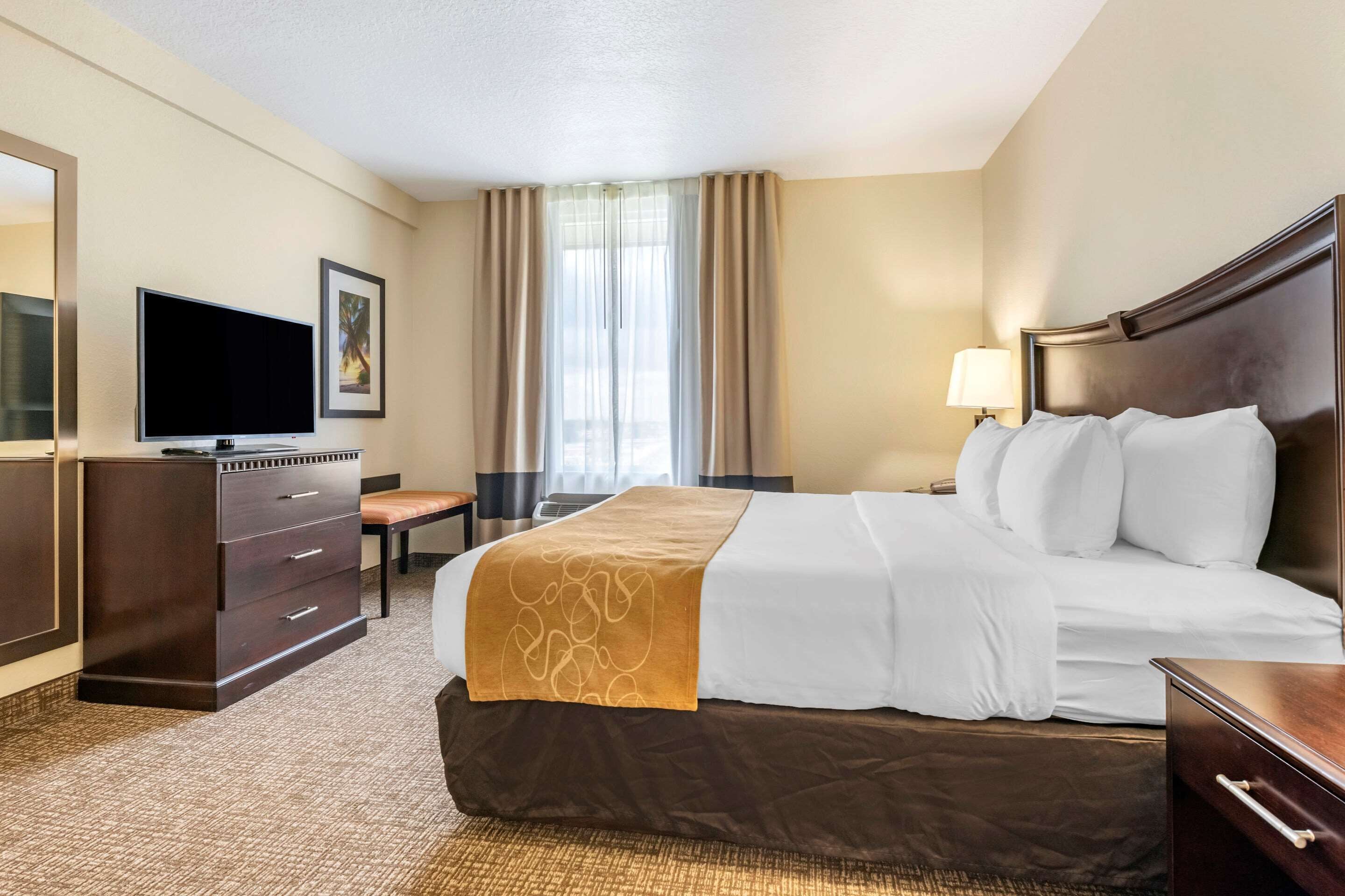 Habitación de hotel con una cama grande, un escritorio con silla, un televisor y una ventana con cortinas.