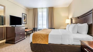 Habitación de hotel con una cama grande, un escritorio con silla, un televisor y una ventana con cortinas.
