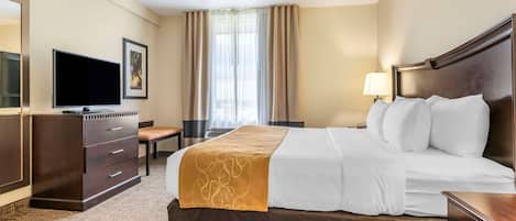 Habitación de hotel con una cama grande, un escritorio con silla, un televisor y una ventana con cortinas.