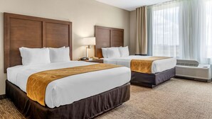 A hotel room with two beds, a large window with curtains, an air conditioning unit, and a bedside table with a lamp. - Comfort Suites Maingate East (Kissimmee)