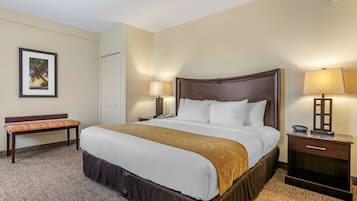 Quarto de hotel com uma cama grande, duas mesas de cabeceira com abajures, um banco e um quadro na parede.