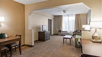 Habitación de hotel con comedor, televisor, escritorio, silla, sofá y ventana con cortinas.