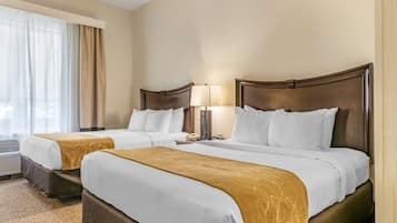 A hotel room with two beds, beige walls, and a large window with curtains.