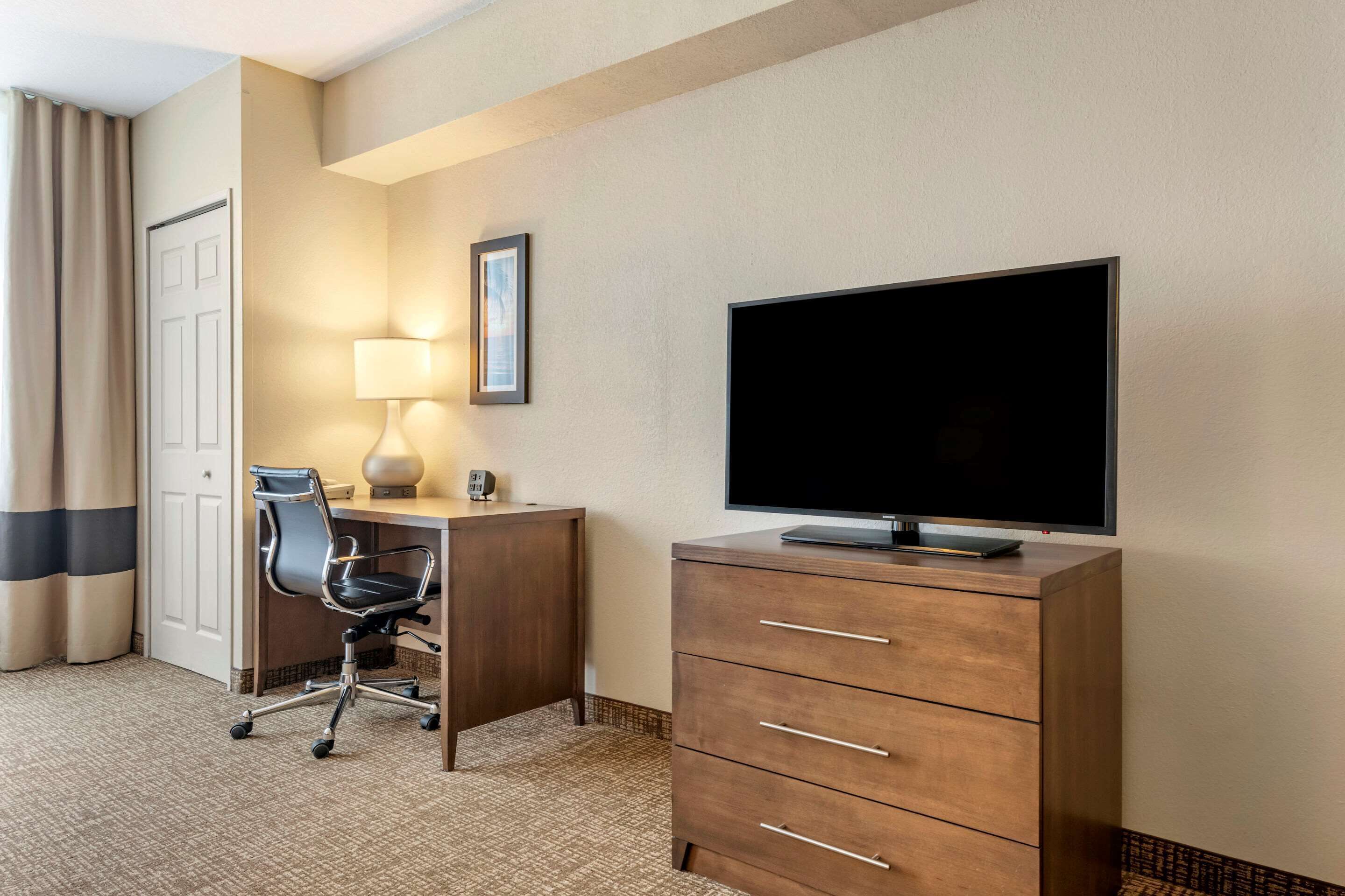 Habitación de hotel con escritorio, silla, televisión y lámpara.