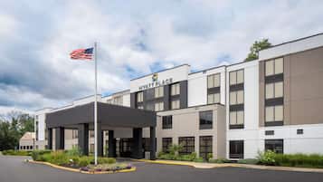 Un hotel moderno Hyatt Place con entrada cubierta, jardín ajardinado y una bandera estadounidense.