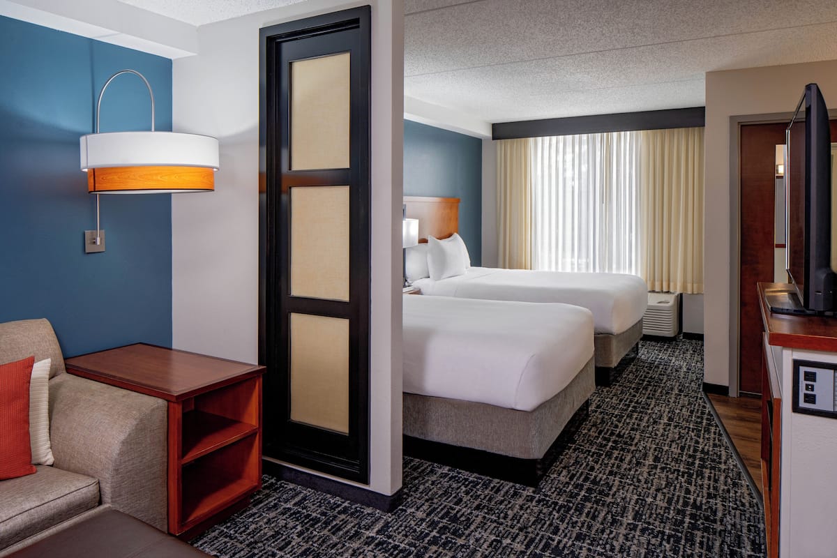 Ein Hotelzimmer mit zwei Betten, einem Schreibtisch, einem Sessel, einer Lampe und einem Fernseher.