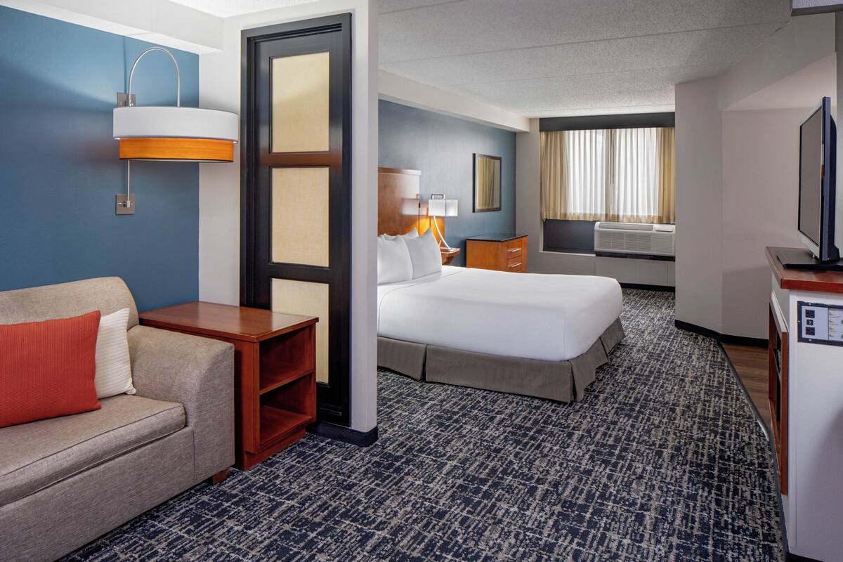 Ein Hotelzimmer mit einem Bett, einer Couch, einem Schreibtisch, einem Fernseher und einem fensterbepflanzten Fenster.