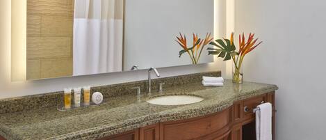 A bathroom with a granite countertop, a sink, a mirror, and wooden cabinets.