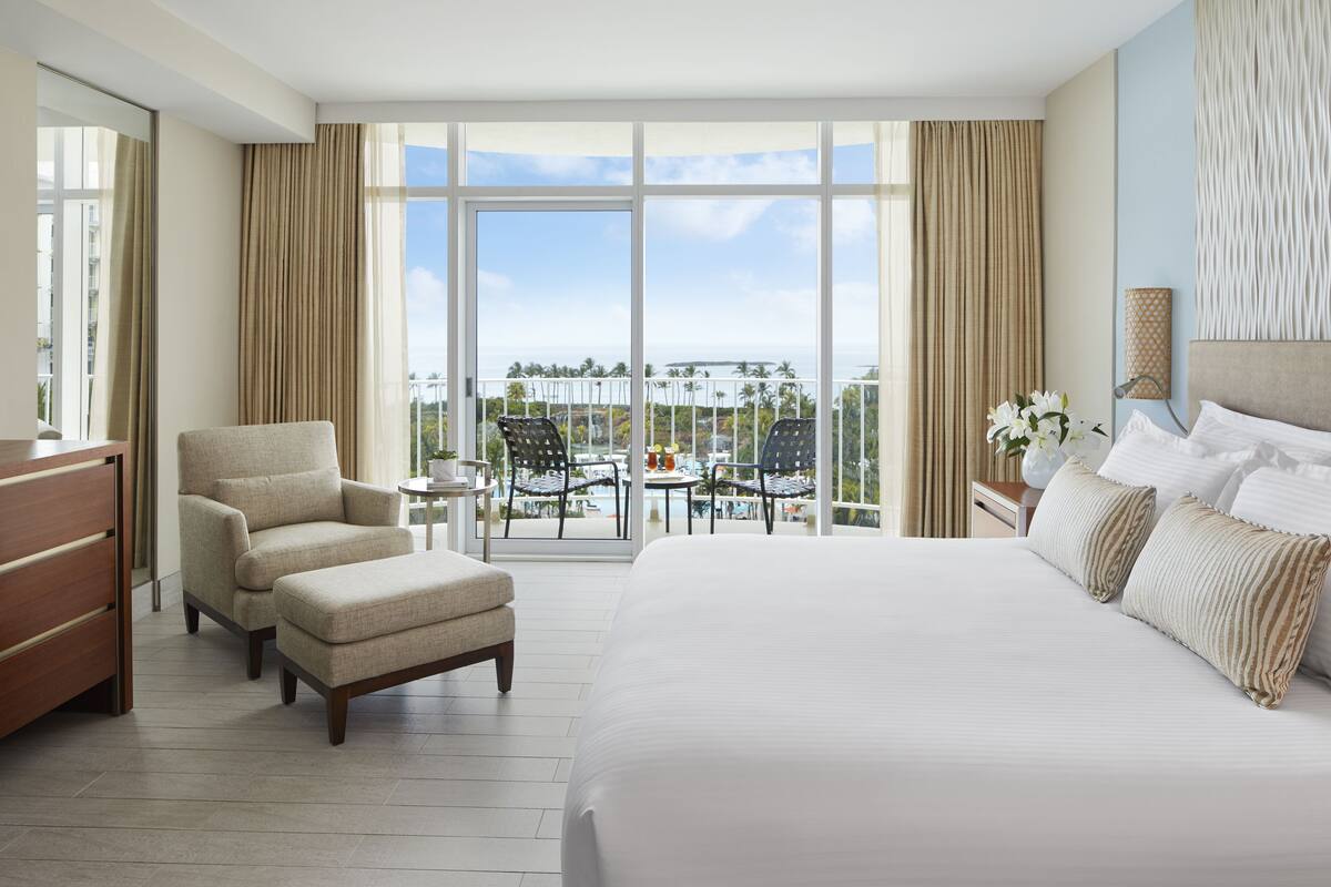 Ein Hotelzimmer mit einem großen Bett, einem Sessel, einem kleinen Tisch und einem Balkon mit Meerblick.