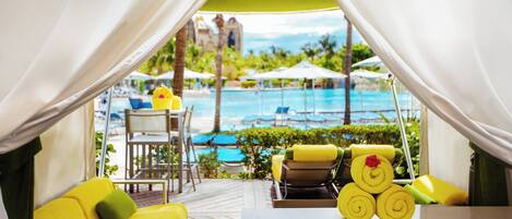 A poolside area with yellow lounge chairs, a table, and a view of a swimming pool and palm trees.