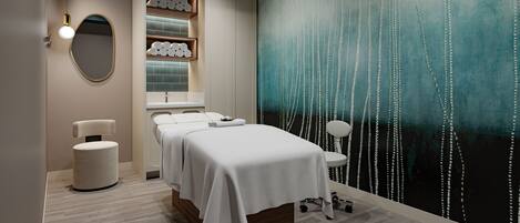 A spa room with a massage table, a wall-mounted shelf with towels, and a large abstract painting.