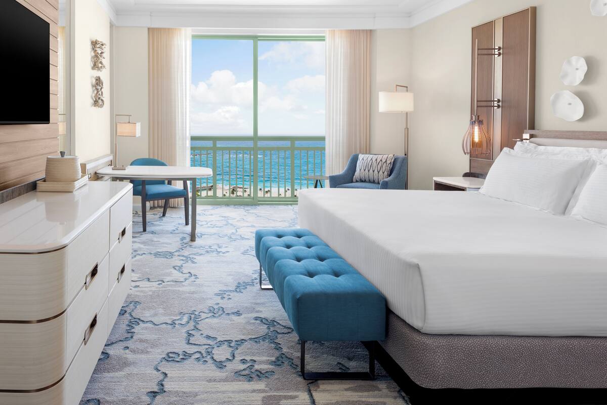 A hotel room with a large bed, a seating area with a table and chairs, a TV, and a view of the ocean.