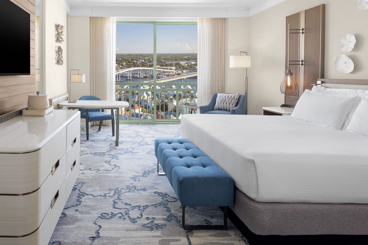 A hotel room with a large bed, a seating area with a view, and a desk with a TV.