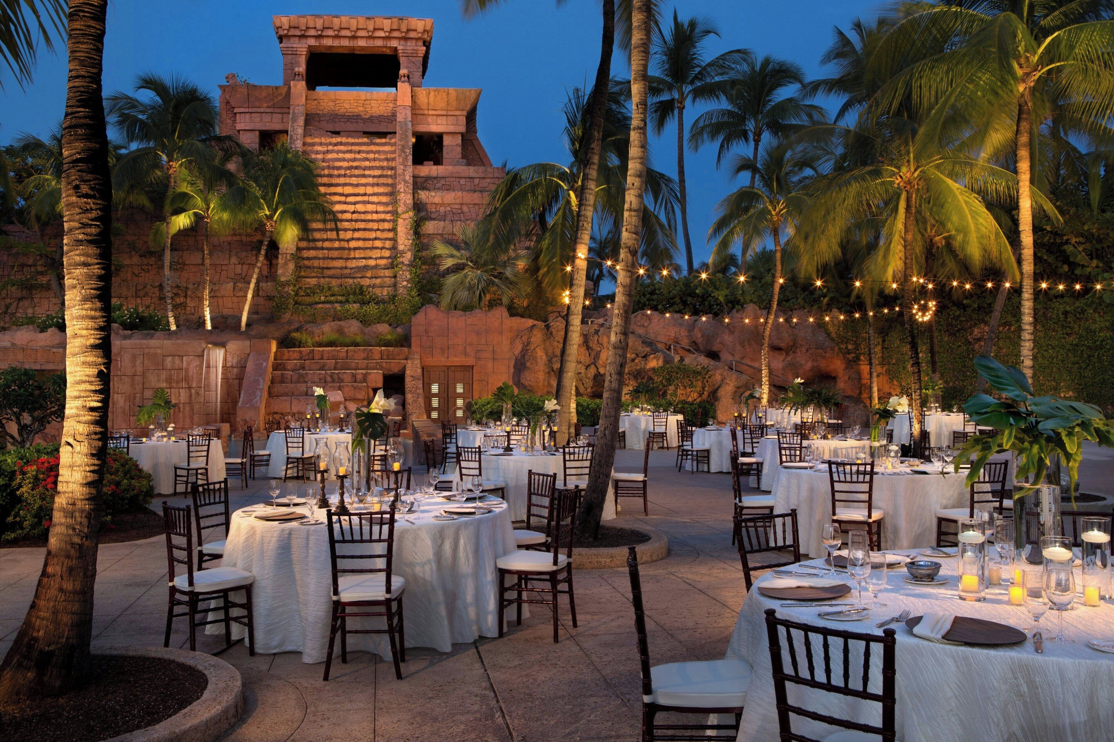 An outdoor dining area with round tables, chairs, and string lights.