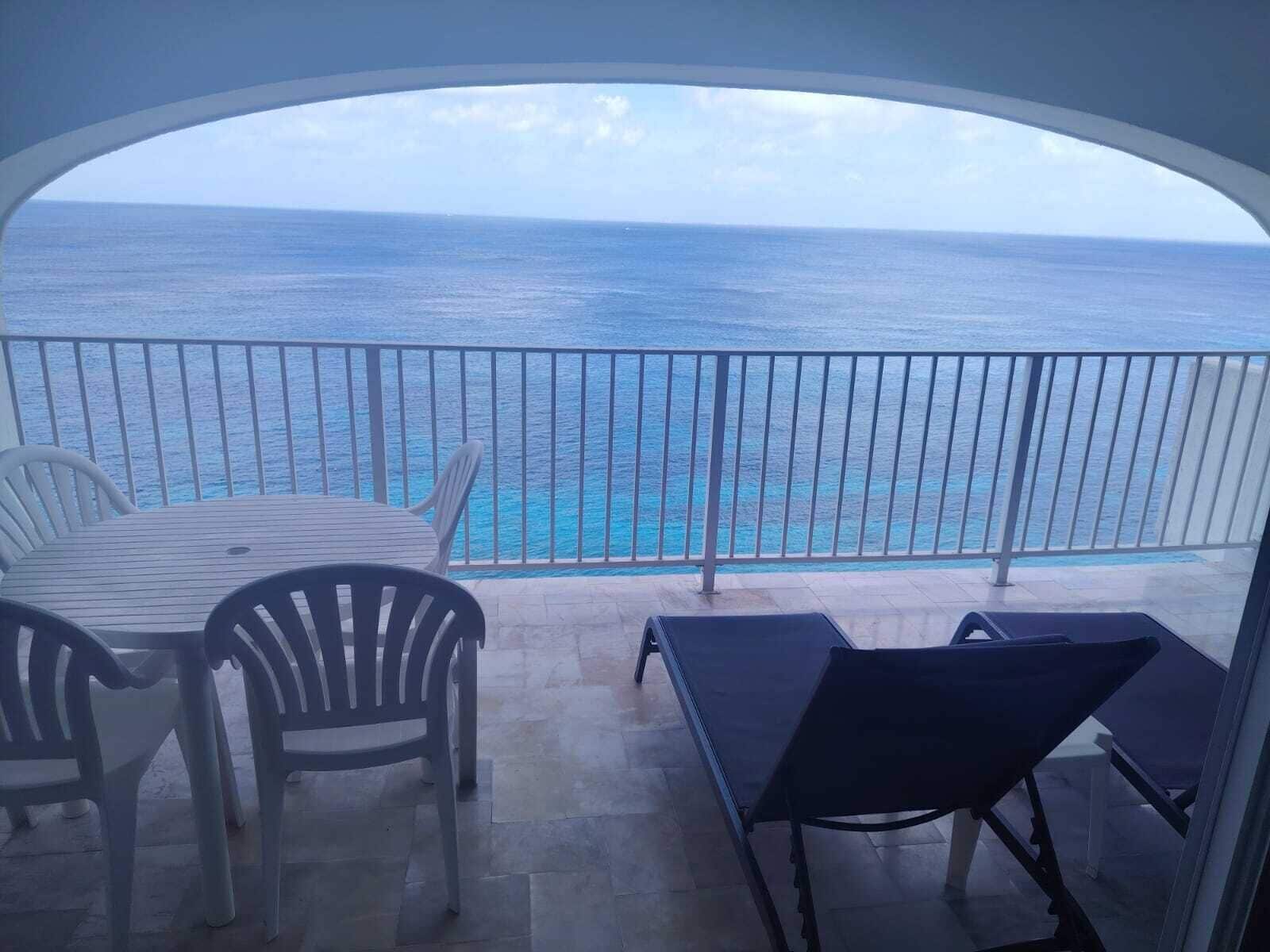 Ein Balkon mit Meerblick, einem Tisch, Stühlen und einer Liege.
