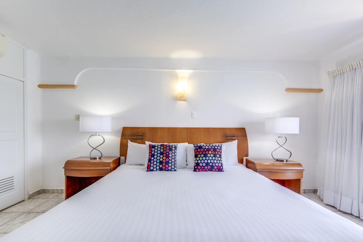Een hotelkamer met een groot bed, twee nachtkastjes met lampen, een houten hoofdbord en een bijzetmeubel met een lamp.