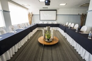 Uma sala de conferências com uma mesa comprida, cadeiras, uma tela de projetor e um centro de mesa decorativo.