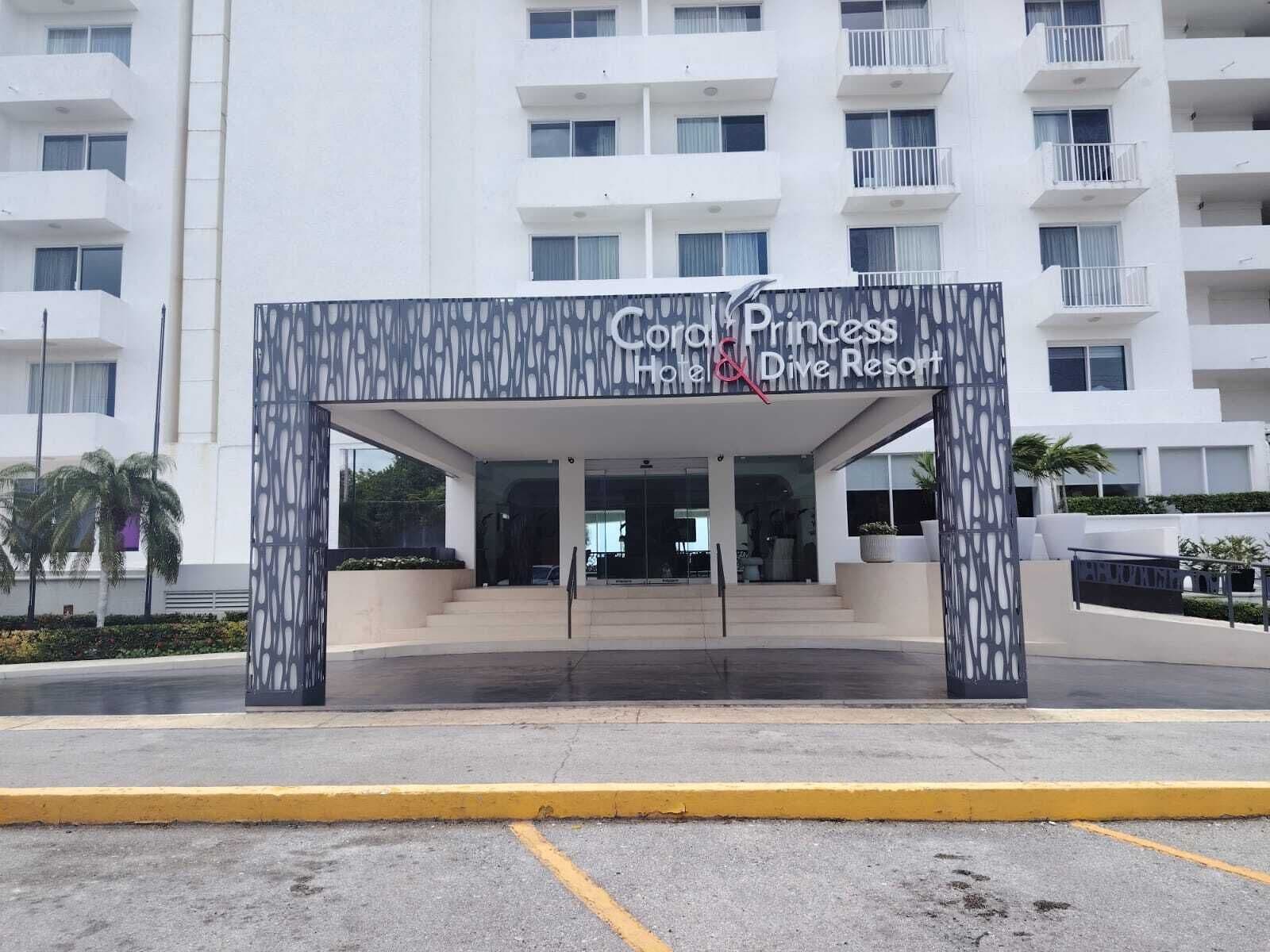 A hotel entrance with a modern design, featuring a sign for 'Coral Princess Hotel & Dive Resort.'