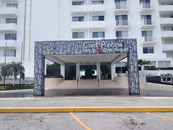 Entrada de hotel con un diseño moderno, que presenta un letrero del 'Coral Princess Hotel & Dive Resort'.