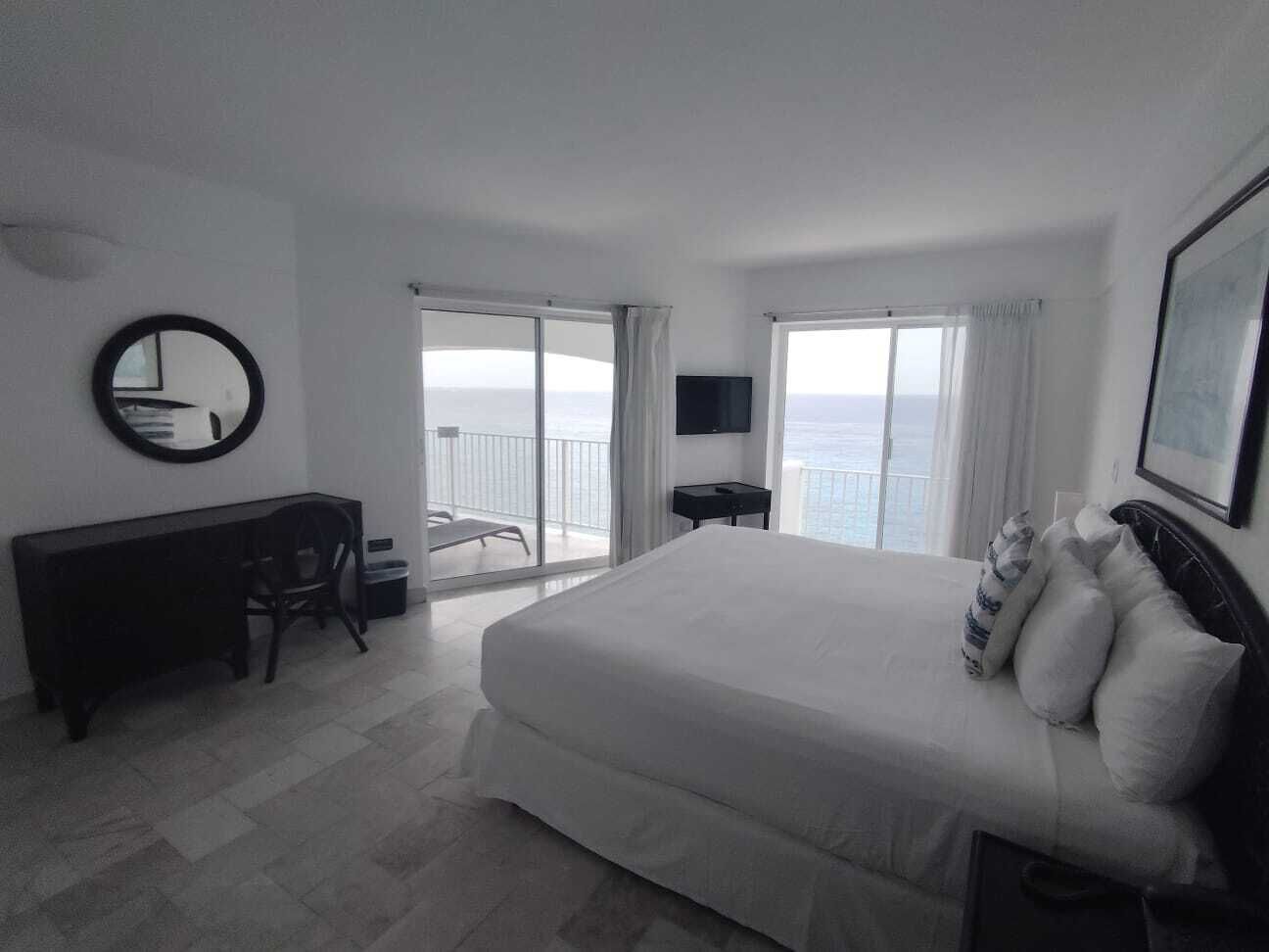 Habitación de hotel con una cama grande, un escritorio, una silla, un televisor y un balcón con vistas.