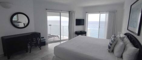 Habitación de hotel con una cama grande, un escritorio, una silla, un televisor y un balcón con vistas.
