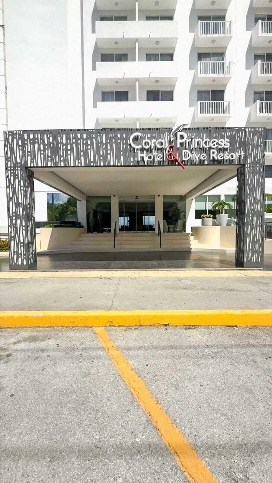 La entrada al Coral Princess Hotel & Dive Resort, con un diseño moderno y una vista despejada de la fachada del edificio.