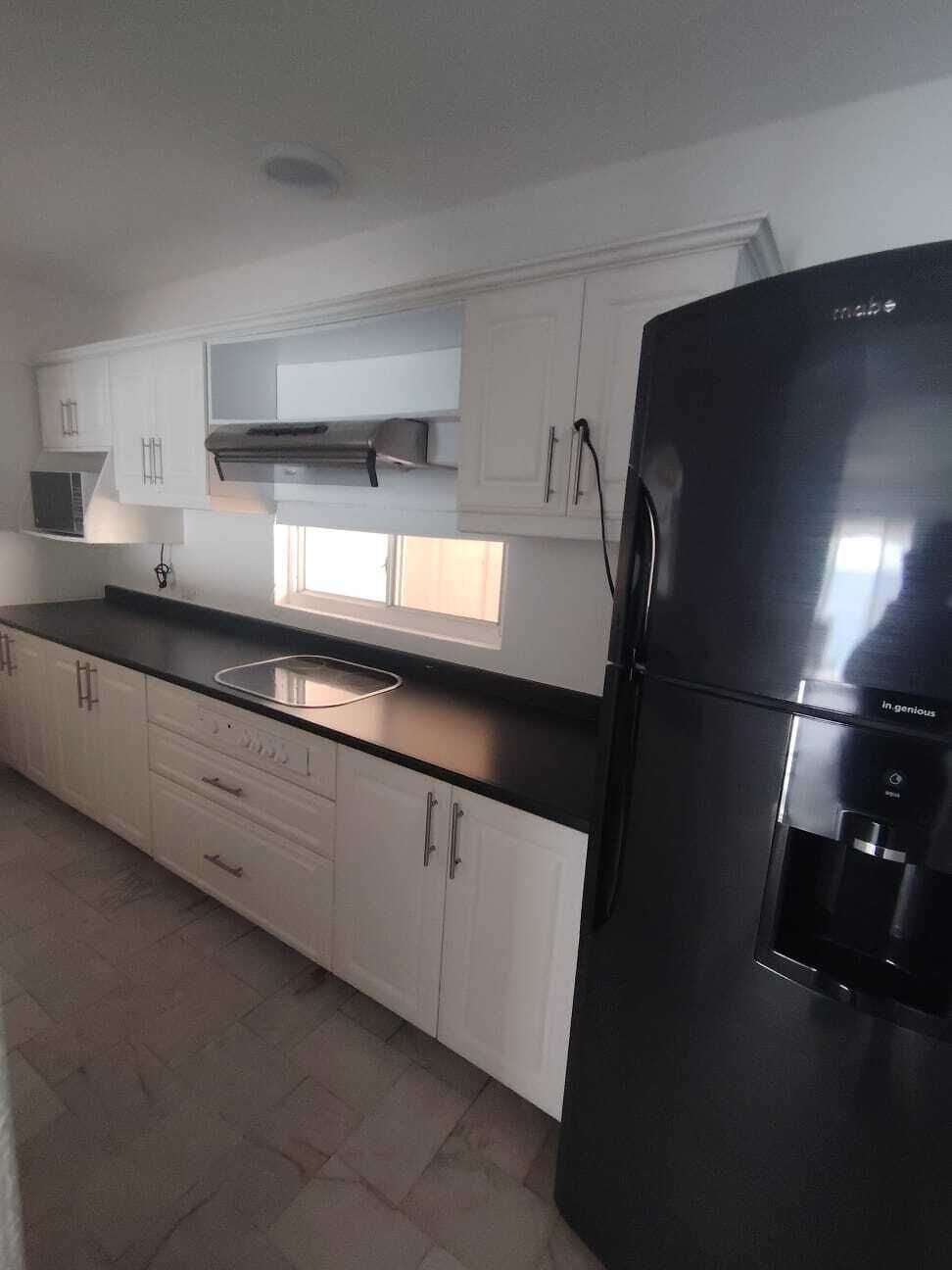 A kitchen with white cabinets, a black refrigerator, and a window above the sink.
