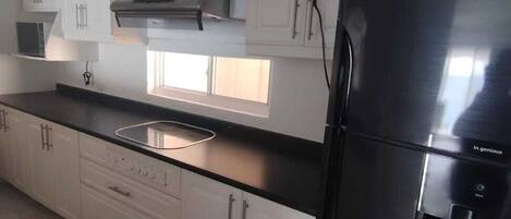 A kitchen with white cabinets, a black refrigerator, and a window above the sink.