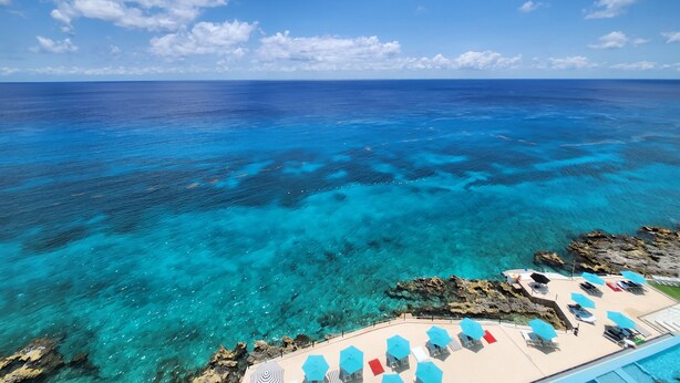 Une vue sur la plage, avec une eau turquoise cristalline, des formations rocheuses et un espace de détente équipé de parasols et de chaises longues.
