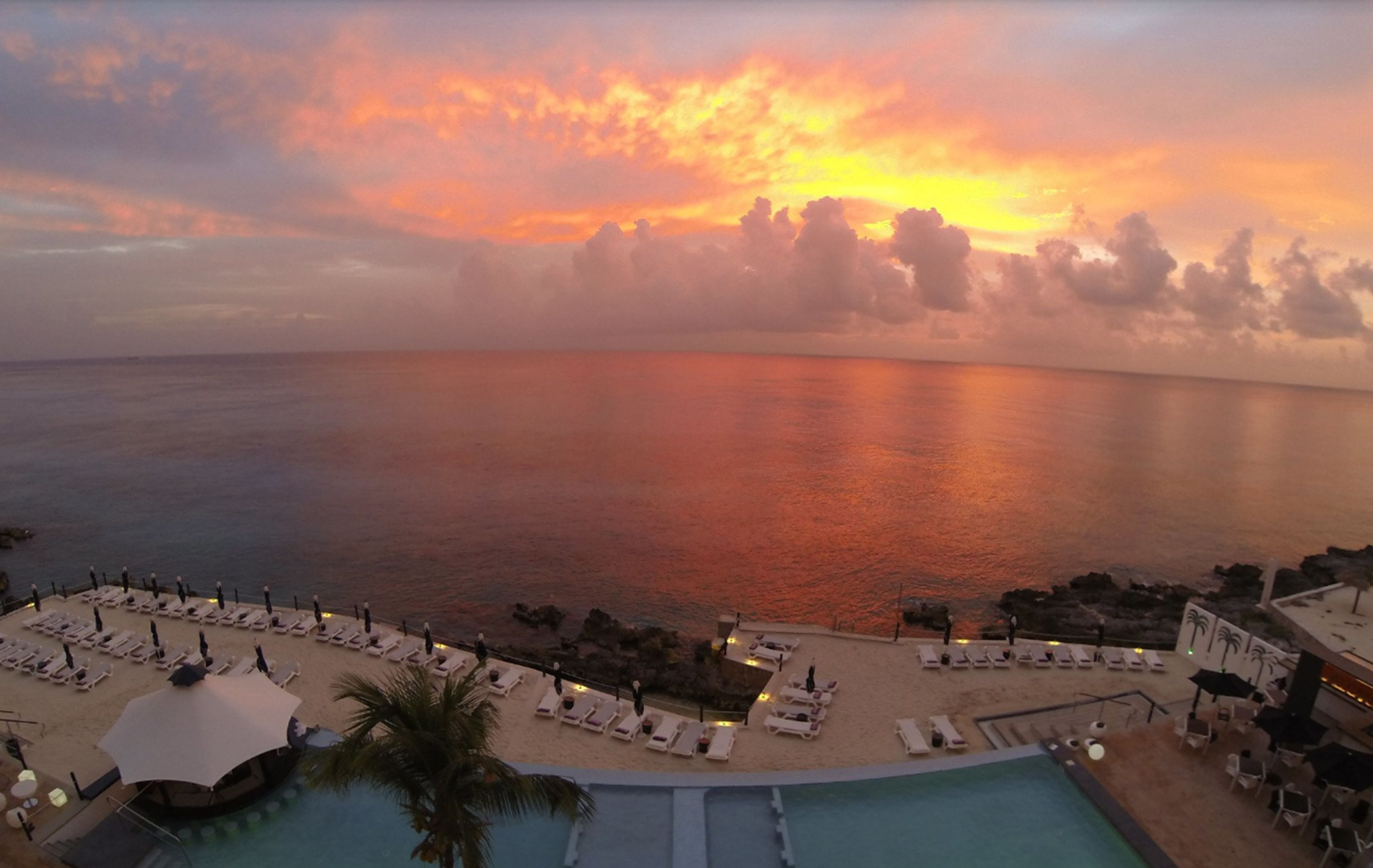 Un resort con piscina, tumbonas y vistas al mar durante el atardecer.