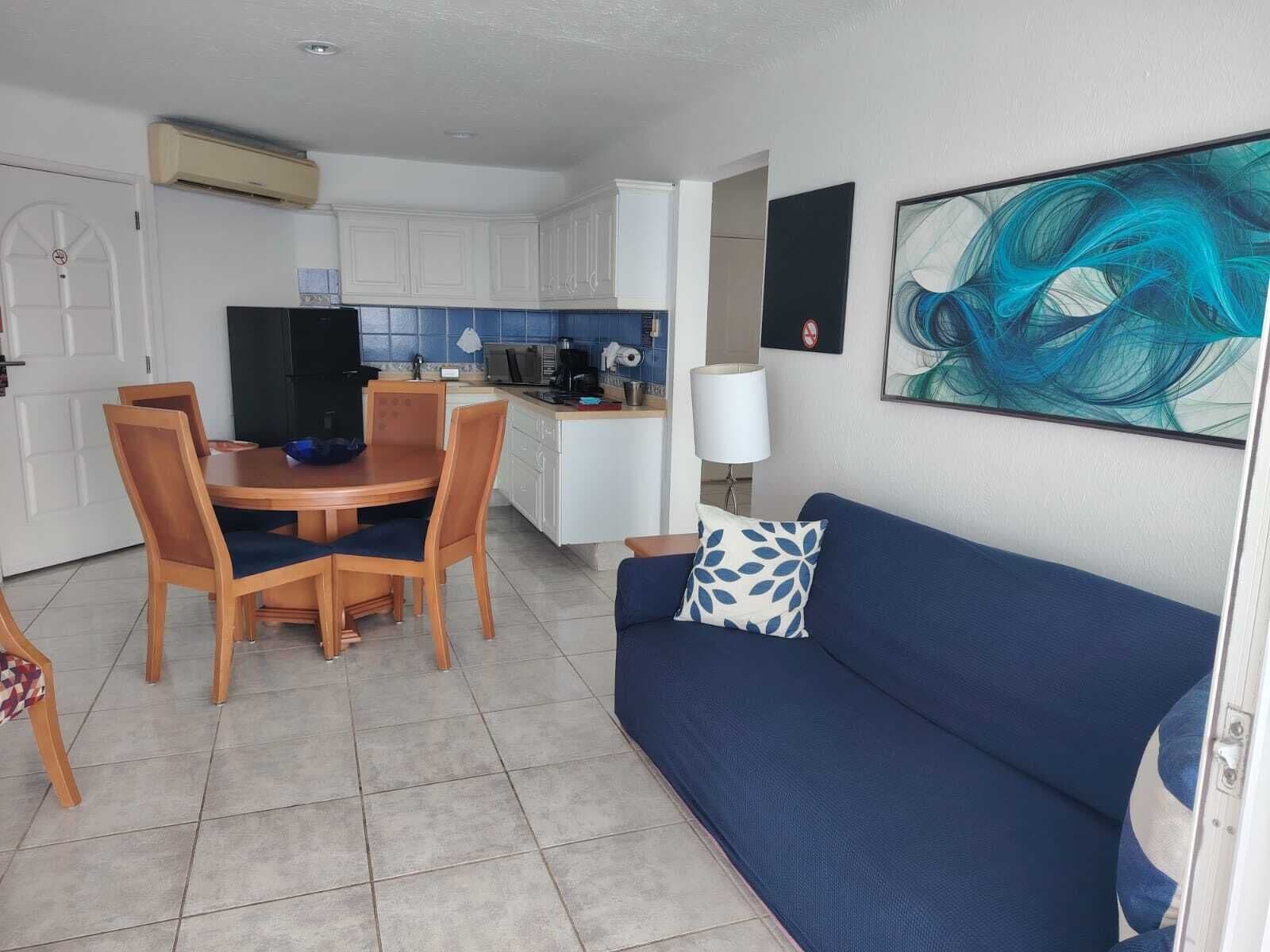 A compact living space with a dining area, kitchenette, and a sofa with a decorative pillow.