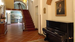 Een statig portaal met een trap, een piano en een portret aan de muur.