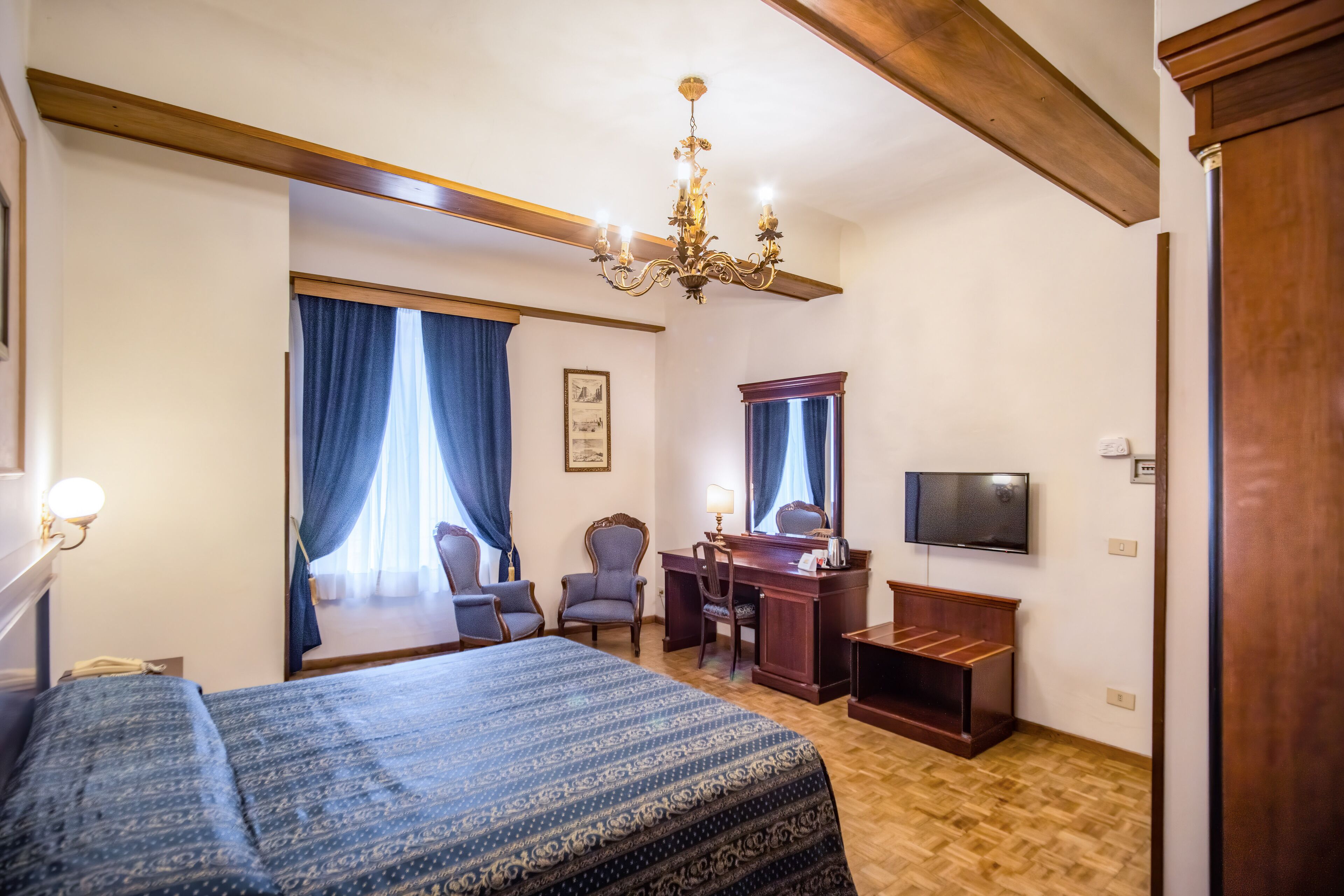 Una camera d'albergo con un letto grande, una scrivania, una sedia, un televisore e un lampadario.