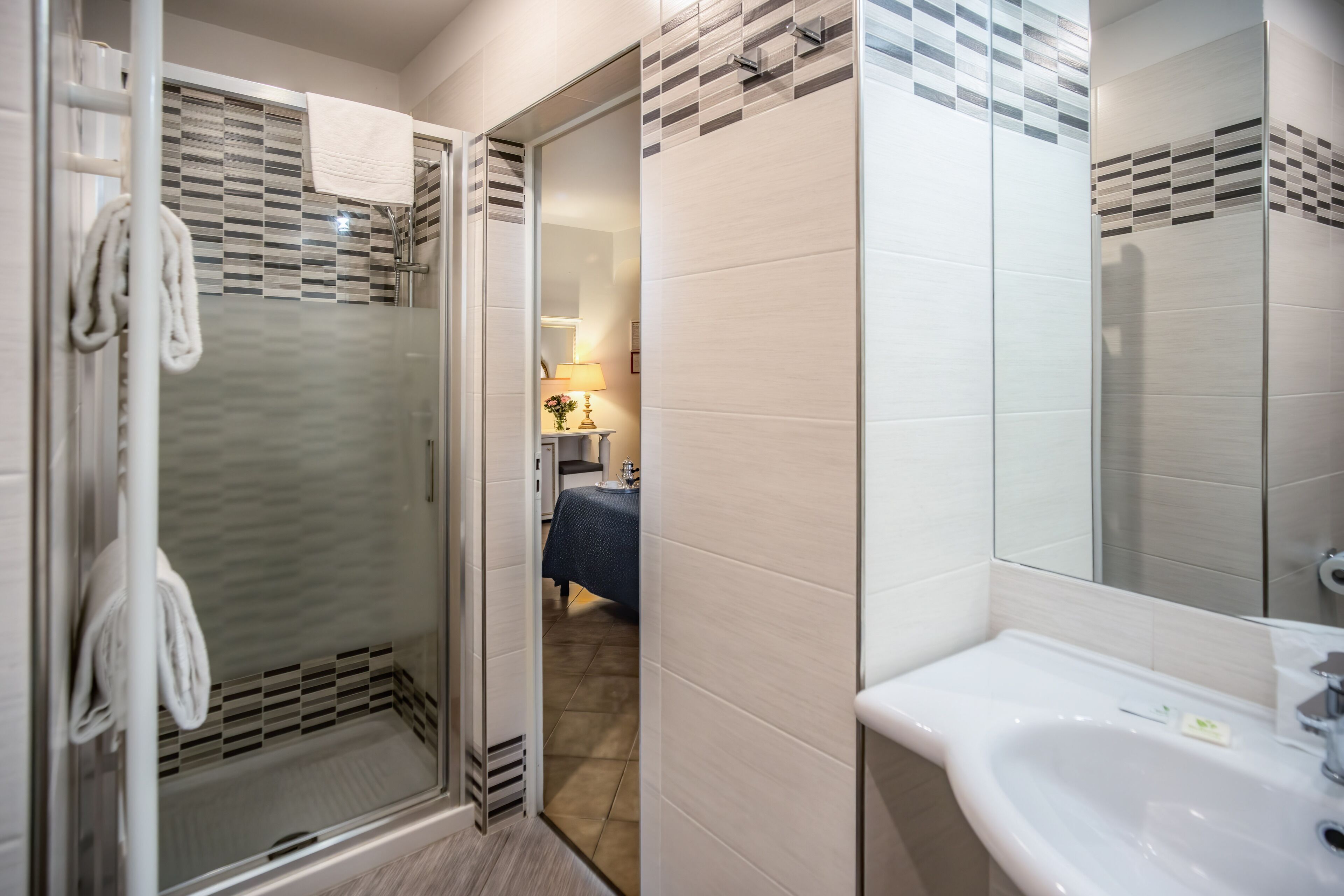 A modern bathroom with a glass shower enclosure, a white sink, and a tiled wall with a geometric pattern.