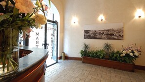 Een hotel lobby met een receptiebalie, een groot raam en een zwart-wit stadsgezicht in een lijst aan de muur.