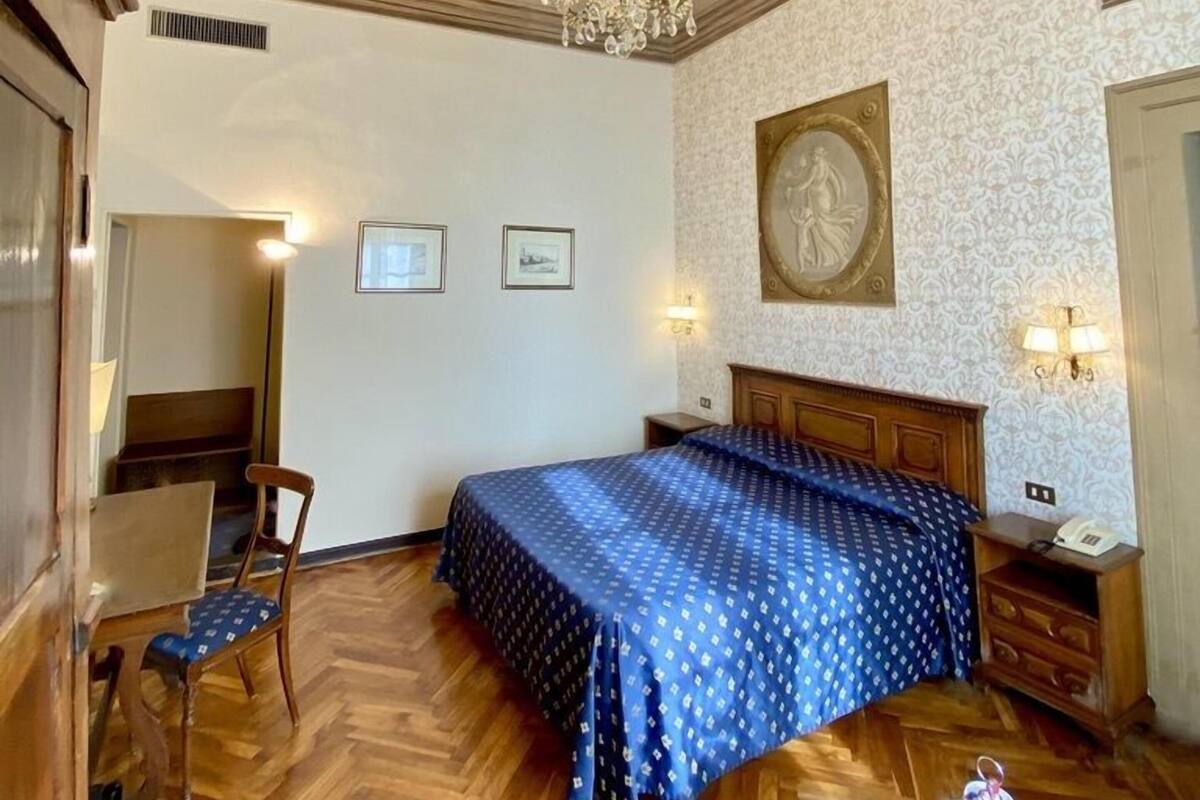 Hotellihuone, jossa on sänky, kattokruunu, puulattia ja koristeltu katto.