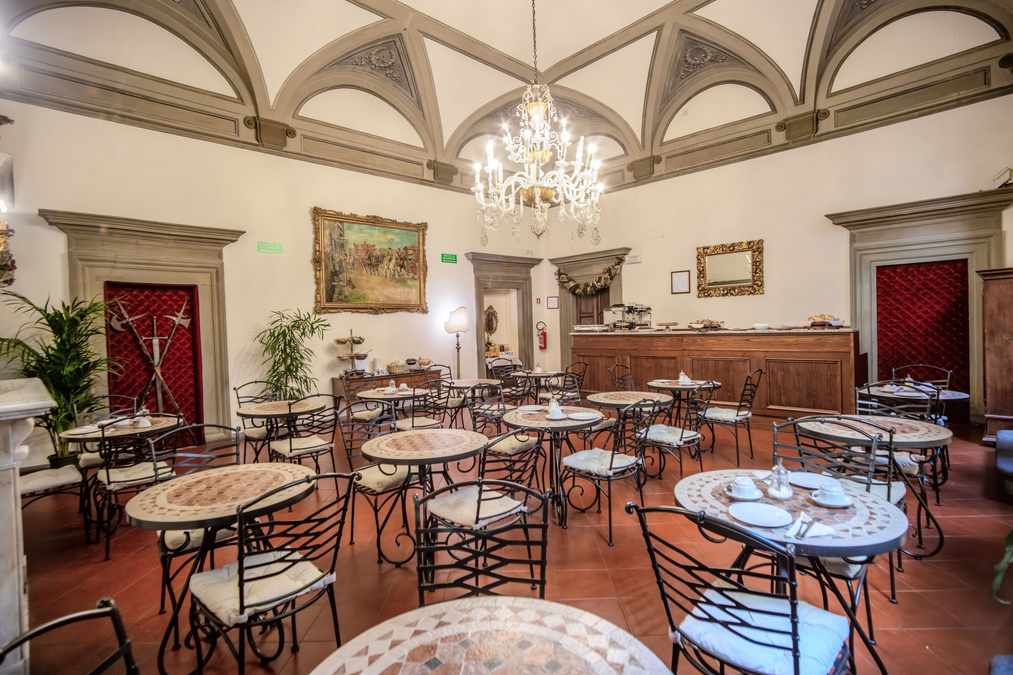A spacious dining area with multiple round tables and chairs, a chandelier, and a bar area.