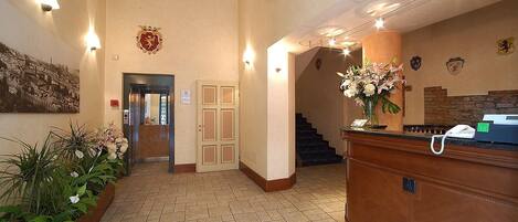 A hotel lobby with a reception desk, a staircase, and a wall-mounted coat of arms.