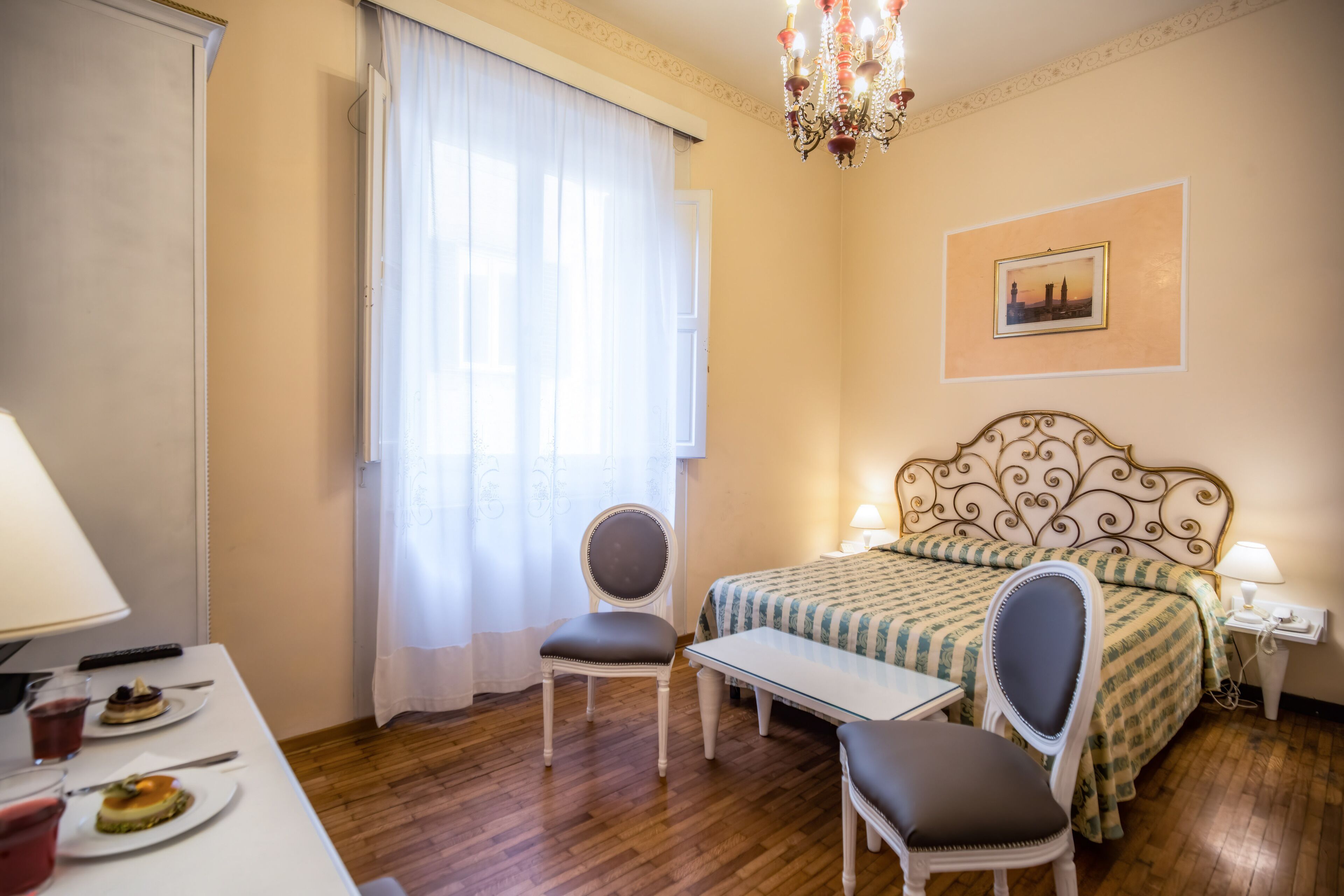 Una habitación de hotel con cama, dos sillones, una mesa y una araña.