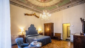 Een hotelkamer met een groot bed, een houten kledingkast, een bureau met telefoon en een kroonluchter.