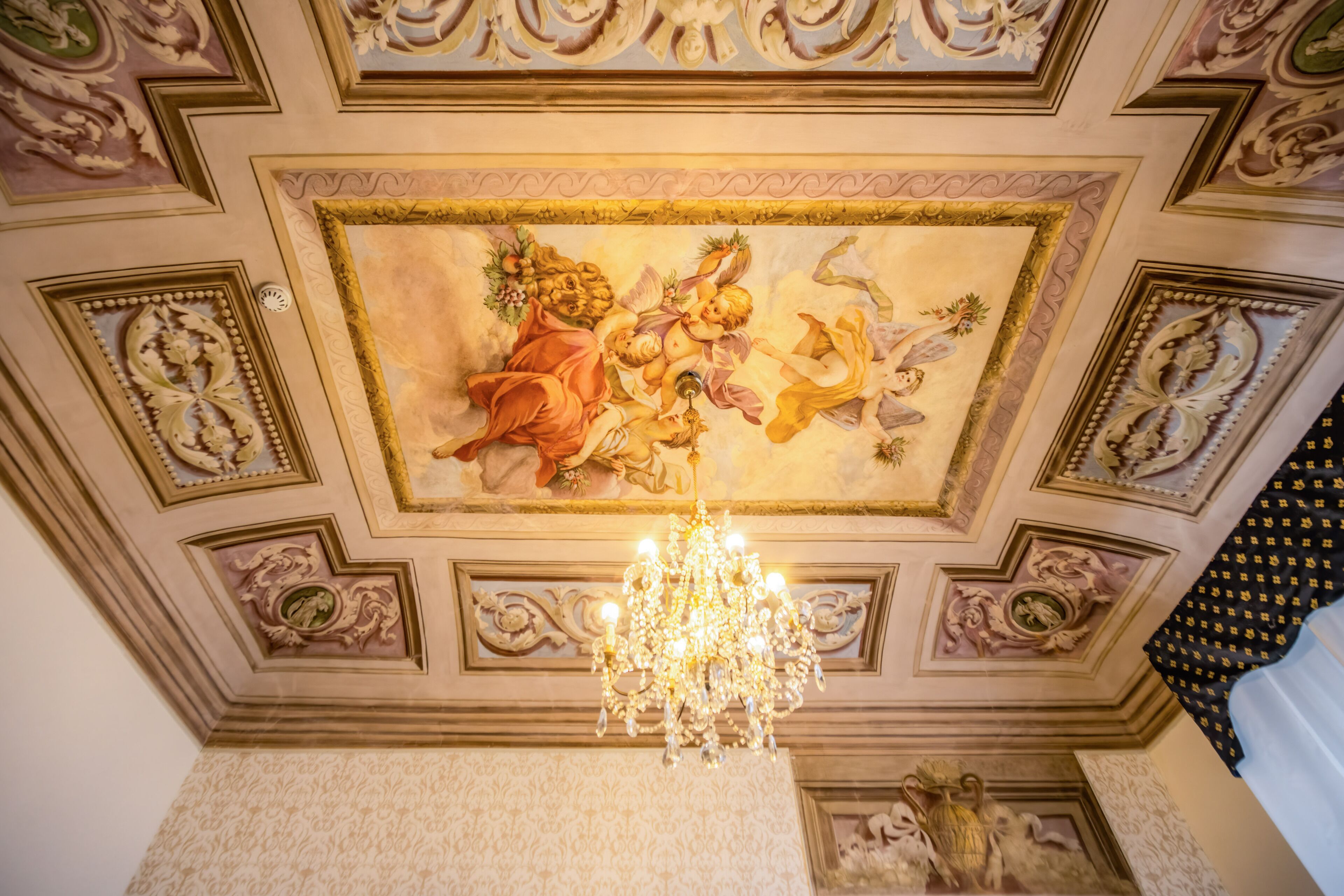 Teto com afresco, um lustre e molduras ornamentadas.