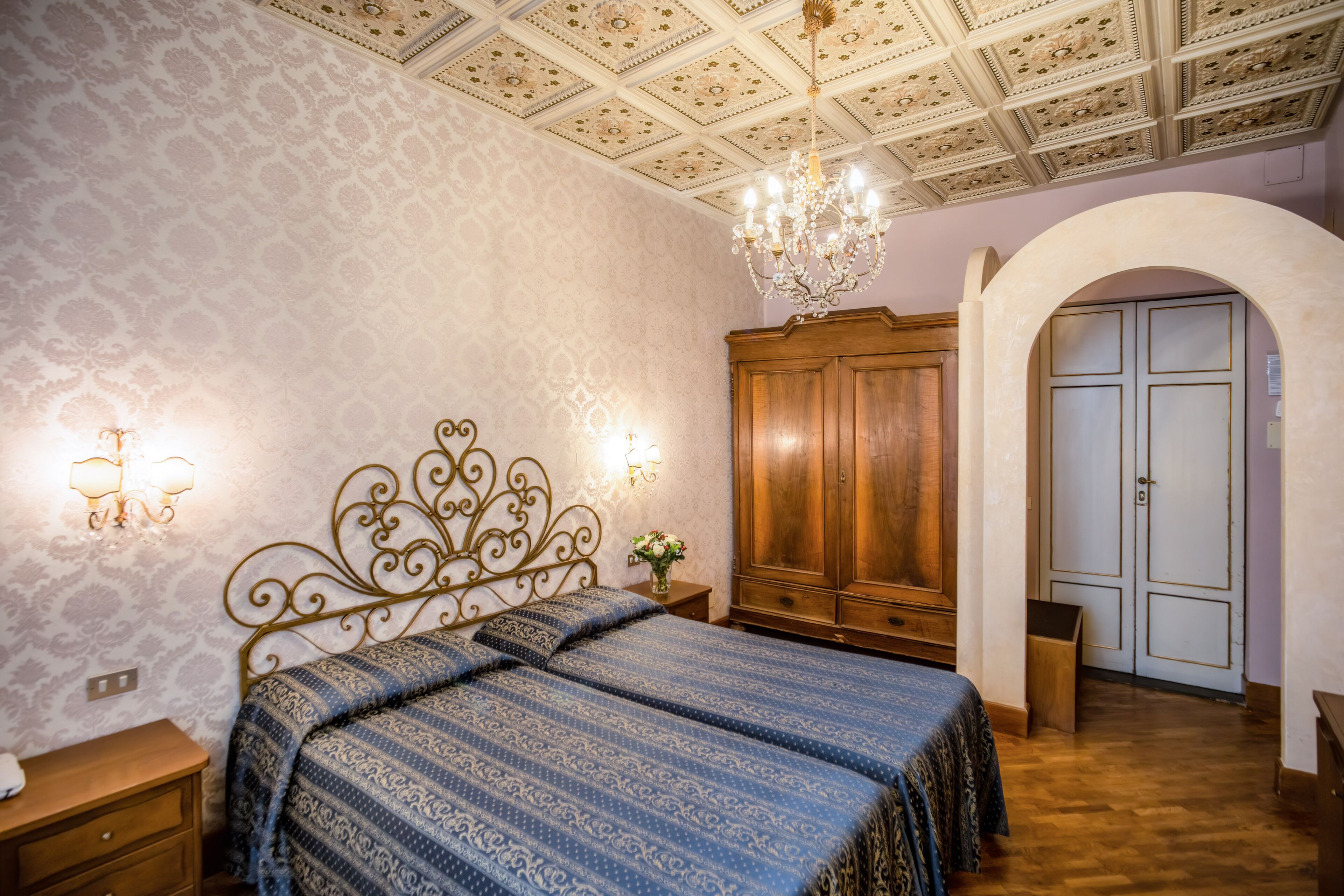 Un dormitorio con colcha estampada, candelabro, armario de madera y una puerta abovedada.