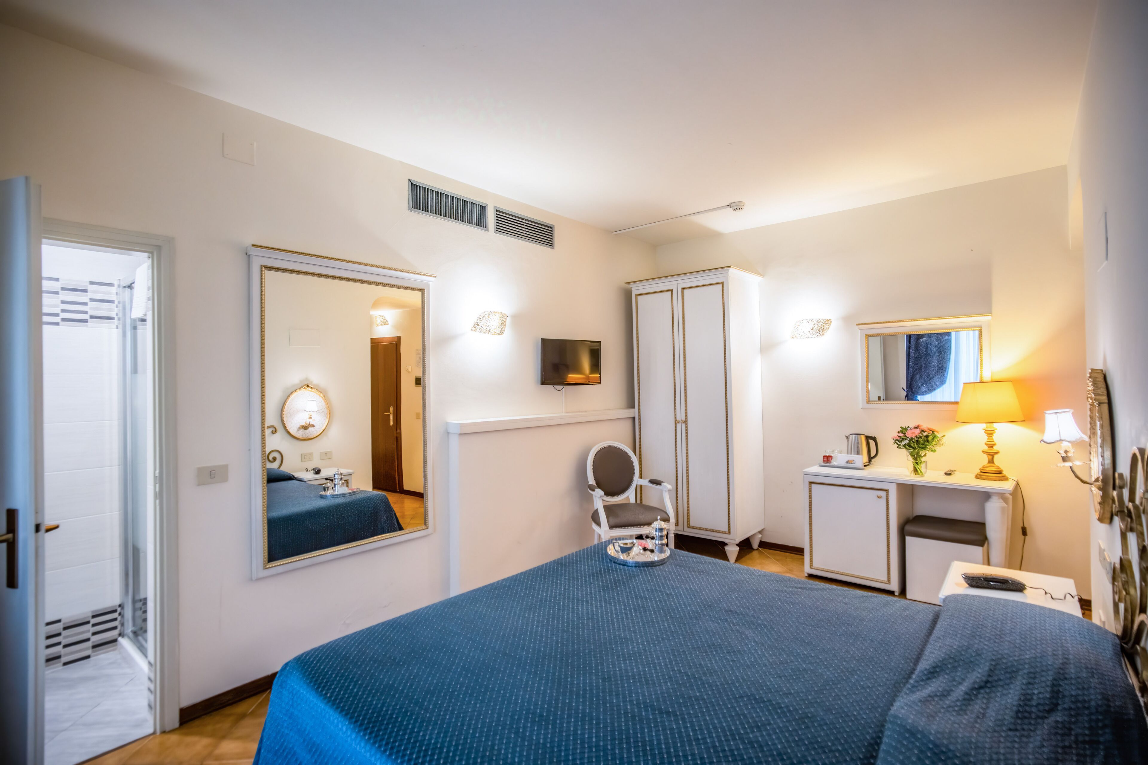 A hotel room with a large bed, a desk with a lamp, a mirror, and a wardrobe.
