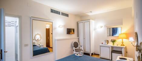 A hotel room with a large bed, a desk with a lamp, a mirror, and a wardrobe.