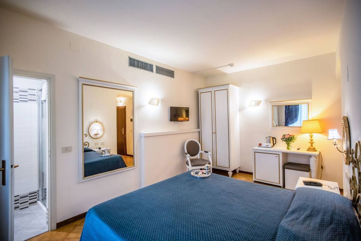 Hotellihuone, jossa on sänky, työpöytä, tuoli, peili, vaatekaappi ja televisio.
