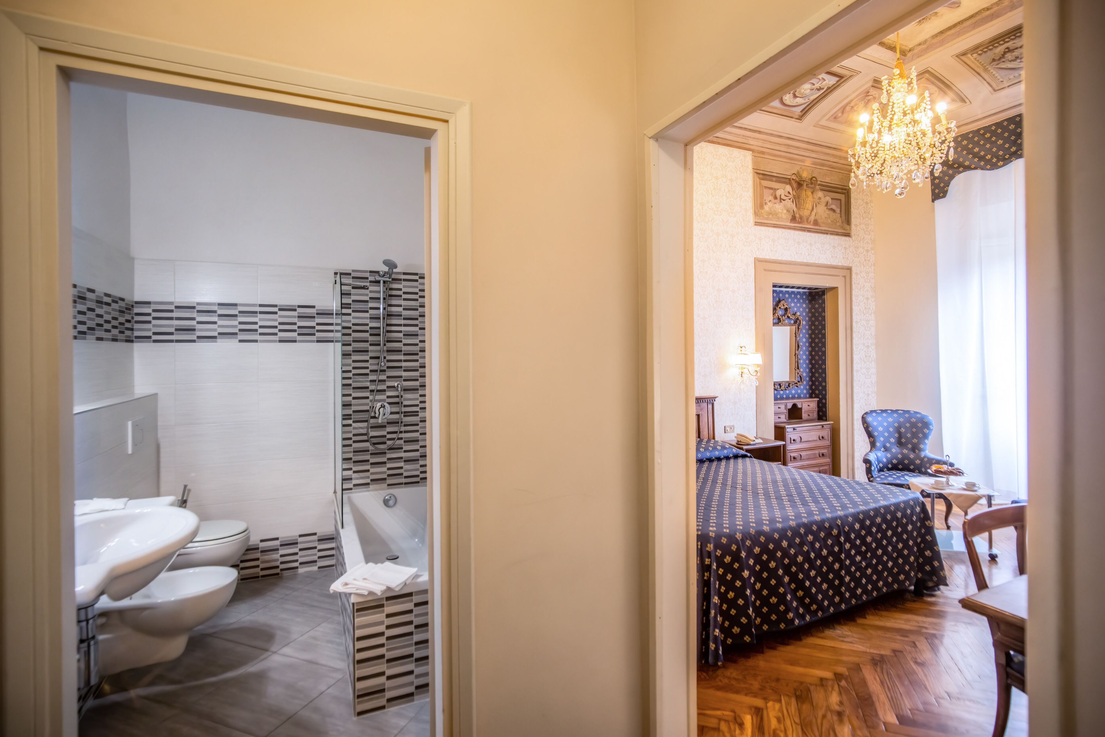 Una habitación de hotel con baño, cama, sillón y candelabro.