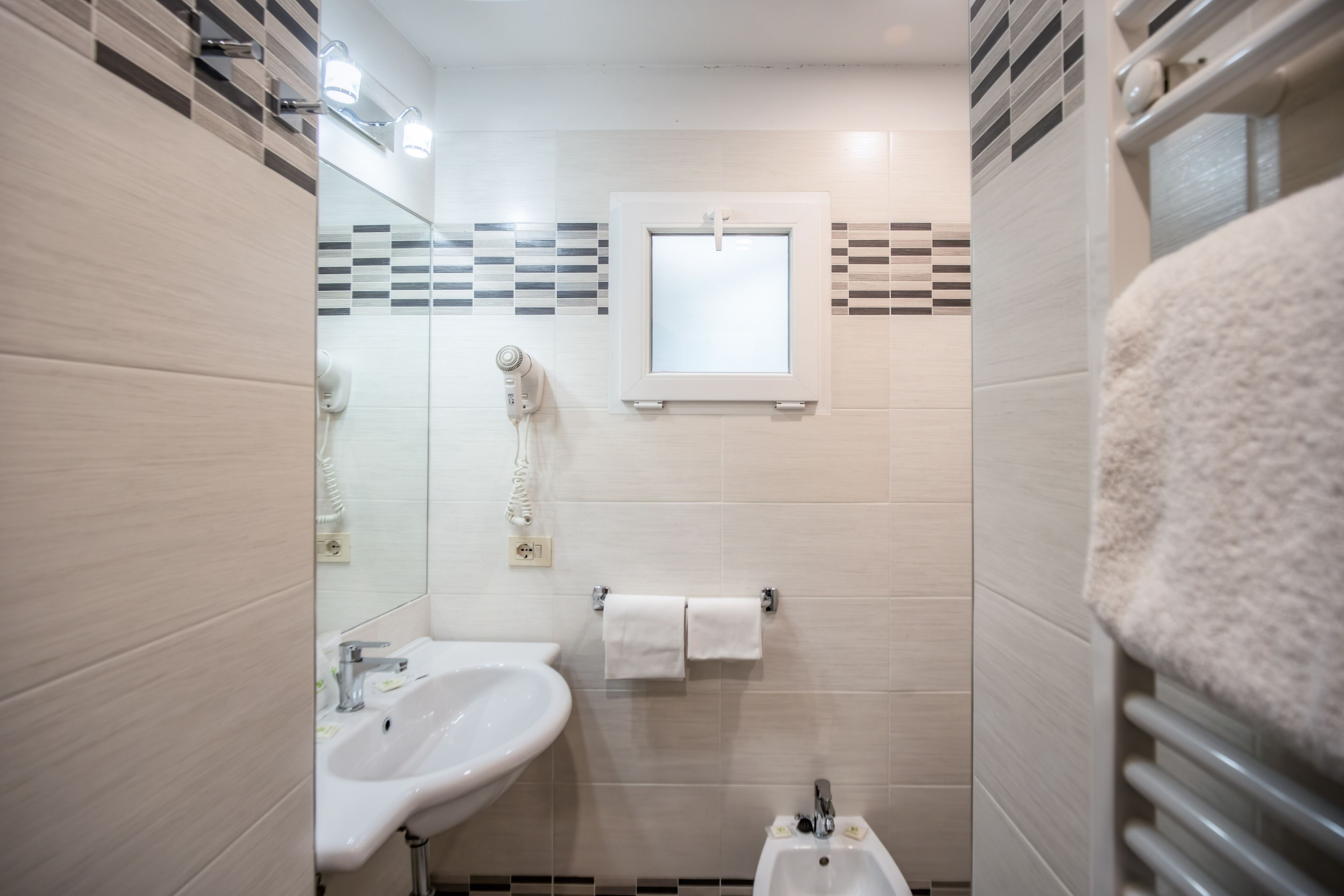 A modern bathroom with a sink, mirror, towel rack, and a small window.