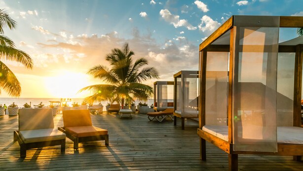 A wooden deck with lounge chairs and a glass-enclosed sleeping area, overlooking the ocean at sunset. - Grand Decameron Montego Beach, A Trademark All Inc (Montego Bay)