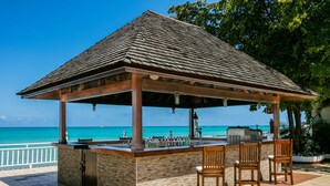 A beachside bar with a tiled floor, a stone counter, and wooden chairs. - Grand Decameron Montego Beach, A Trademark All Inc (Montego Bay)