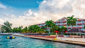 A resort with a pool, palm trees, and a building with balconies. - Grand Decameron Montego Beach, A Trademark All Inc (Montego Bay)